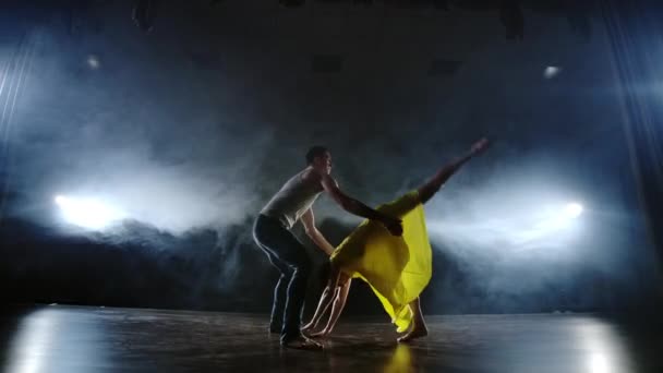 Масштабна камера, дві сучасні балетні танцівниці танцюють на сцені в диму, чоловік піднімає свого партнера на руках і обертається в повітрі. Музика використовує циркових артистів-акробатів — стокове відео