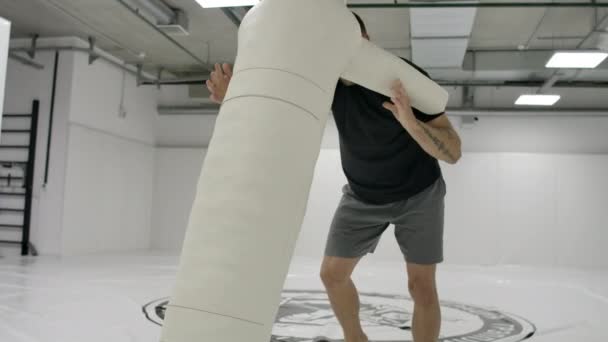 Ein Mann im schwarzen T-Shirt wirft mit einer Vogelscheuche auf das Tatami — Stockvideo