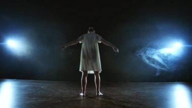 Beyaz kısa elbiseli modern kız dansçı plastik güzel dramatik danslar gerçekleştirir, sahne boyunca çalışan, yere düşen ve iplik. Fenerler ve duman