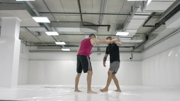 Zwei männliche Ringer in einem weißen Raum trainieren Wurfmatten. Greifen Sie zu und werfen Sie sich durch — Stockvideo