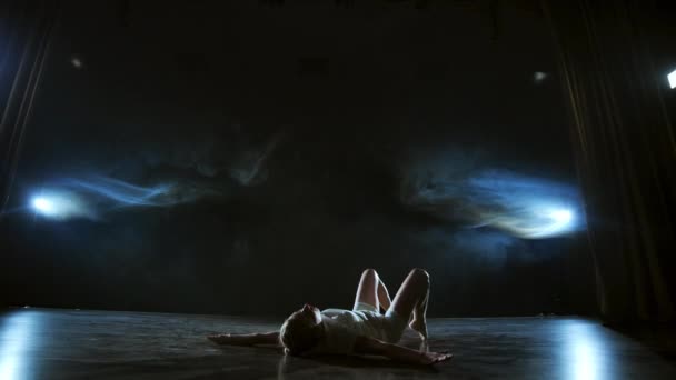 Danza moderna donna in abito bianco balla un balletto moderno, salta, fa rotazione sul palco con il fumo sotto i riflettori blu . — Video Stock