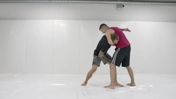 Dois lutadores masculinos em uma sala branca trabalham jogando tapetes. Pegue uma garra e jogue através de si mesmo — Vídeo de Stock