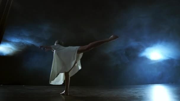 Жінка в білій сукні танцює на сцені драматичні танці сучасного балету. Балетмейстер рухає пластик, виконуючи сучасну хореографію в диму — стокове відео