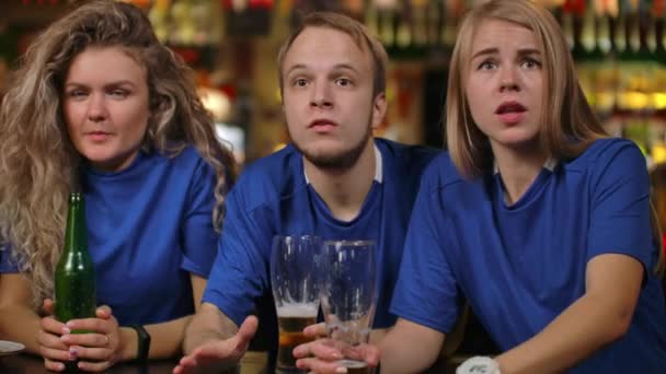 Närbild grupp av fans känslomässigt titta på en sport sänds i en bar på TV med öl, män och kvinnor i blå T-shirts av olika raser, är upprörda efter att ha förlorat och förlorat sitt lag — Stockvideo