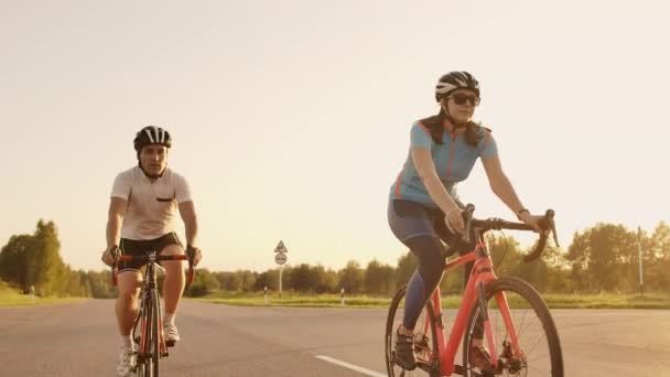Σταθερό σφηνάκι δύο υγιή μεμ και γυναίκα πουλώντας γρήγορα με Ποδηλασία οδικό ποδήλατο στο ηλιοβασίλεμα. — Αρχείο Βίντεο