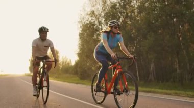 Bir adam ve bir kadın yavaş hareket 120 fps vites ve koruyucu kask gün batımında karayolu üzerinde spor bisiklet binmek