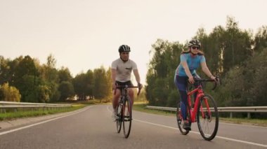 Bisikletli bir erkek ve bir kadın gün batımında birlikte yavaş çekimde yolda dırlar. Çift Bisiklet ile seyahat. Spor Bisiklet kask