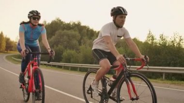 Bisikletli bir erkek ve bir kadın gün batımında birlikte yavaş çekimde yolda dırlar. Çift Bisiklet ile seyahat. Spor Bisiklet kask