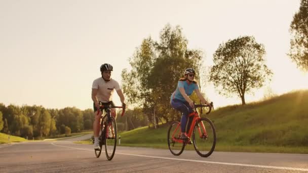 Gün batımında bisiklet yol bisikleti ile hızlı satarak iki sağlıklı mem ve kadın Steadicam çekim. — Stok video