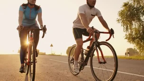 Bir adam ve bir kadın yavaş hareket 120 fps vites ve koruyucu kask gün batımında karayolu üzerinde spor bisiklet binmek — Stok video