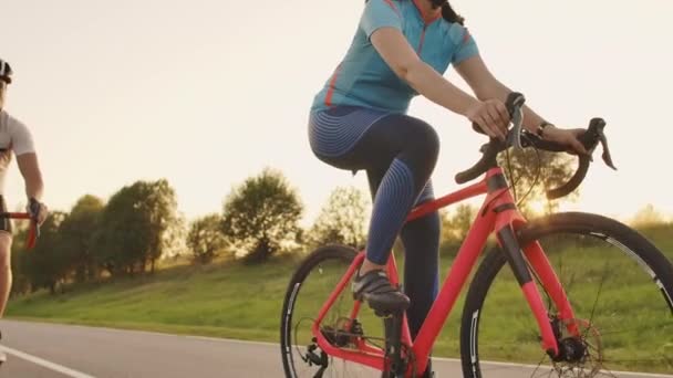 Two cyclists a man and a woman ride on the highway on road bikes wearing helmets and sportswear at sunset in slow motion. — Stock Video