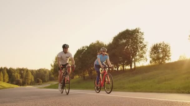 自転車に乗った男女がスローモーションで日没時に一緒に道路を下りる。夫婦は自転車で旅行する。スポーツサイクリングヘルメット — ストック動画