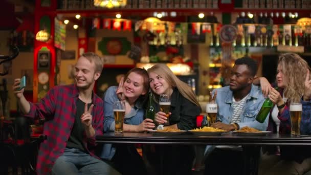 In der Bar oder im Restaurant macht der hispanische Mann ein Selfie von sich und ihren besten Freundinnen. Schöne junge Leute in stilvollem Lokal — Stockvideo