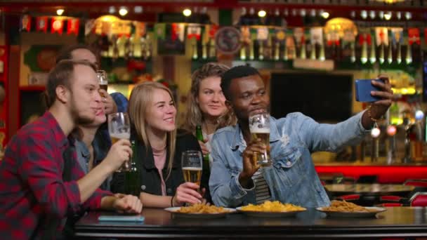 In der Bar oder im Restaurant macht der hispanische Mann ein Selfie von sich und ihren besten Freundinnen. Schöne junge Leute in stilvollem Lokal — Stockvideo