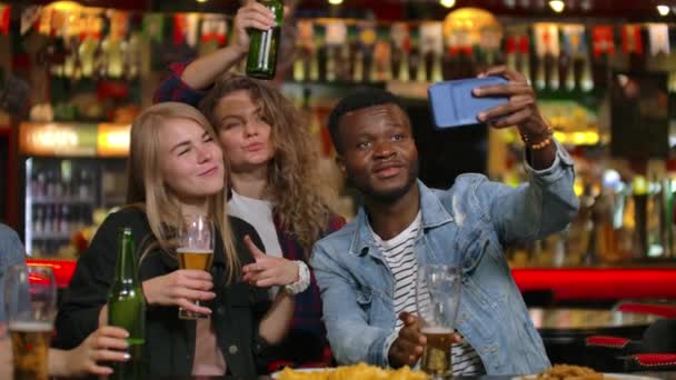 Un grupo de amigos multiétnicos descansando en el bar. Los amigos toman una foto en el teléfono en el bar, hacen una foto compartida en el teléfono. Fiesta con amigos en el bar con cerveza — Vídeos de Stock