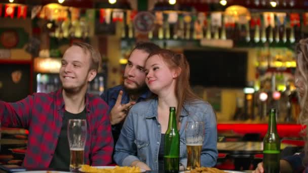 Un grupo de amigos multiétnicos descansando en el bar. Los amigos toman una foto en el teléfono en el bar, hacen una foto compartida en el teléfono. Fiesta con amigos en el bar con cerveza — Vídeos de Stock