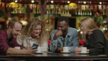 Mutlu çok ırklı arkadaş grubu akıllı telefonlar kullanarak konuşuyor. Kafede akıllı telefonlar kullanarak konuşan mutlu çok ırklı arkadaş grubu, farklı gençler.