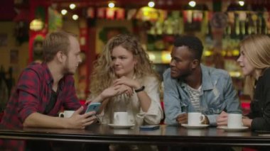 Kafede otururken akıllı telefon bakarak neşeli genç arkadaşlar Portresi. Karışık ırk insanlar cep telefonu kullanarak restoranda bir masada oturan.