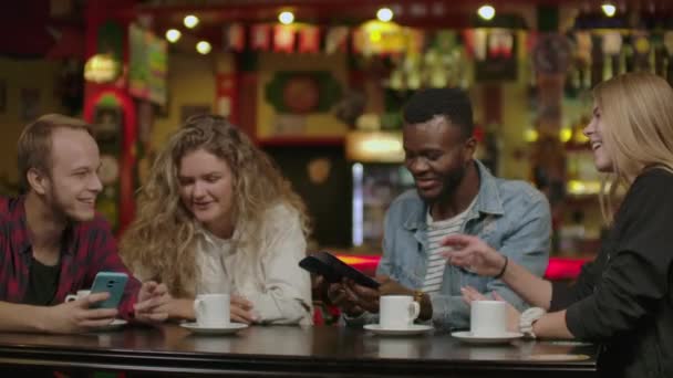 Mooie Spaanse man toont interessante dingen op haar Smartphone aan haar vrienden, terwijl ze hebben goede tijd in bar. Ze lachen, grap, drinken in stijlvolle hipster Bar etablissement — Stockvideo