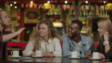 Kafede otururken akıllı telefon bakarak neşeli genç arkadaşlar Portresi. Karışık ırk insanlar cep telefonu kullanarak restoranda bir masada oturan.