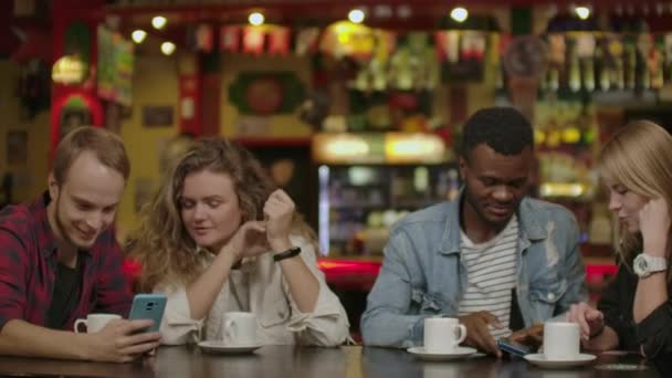 Piękny Hiszpan pokazuje ciekawe rzeczy na jej smartphone do jej przyjaciół, podczas gdy mają dobry czas w barze. Śmiech, Joke, drink w stylowym Hipster bar ustanowienie — Wideo stockowe