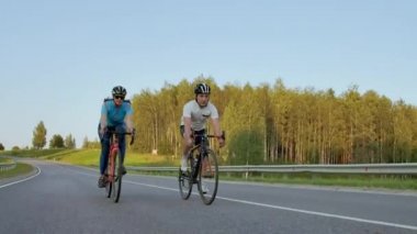 İki profesyonel yol bisikletçisi bisikletlerini bir tepede sürerler. Sıcak ama rüzgarlı bir yaz gününde eğitim iki güçlü bisikletçiler kadın ve erkek El düzenlenen atış.