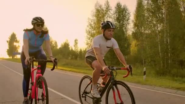 Vista frontal de una joven pareja o amigos montando sus bicicletas en el parque o bulevar de la ciudad en verano. Concepto de personas, ocio y estilo de vida . — Vídeo de stock