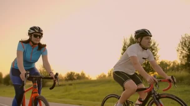 Dois ciclistas profissionais andam de bicicleta numa colina. Mão tiro realizado de dois ciclistas fortes do sexo feminino e masculino em seu treinamento em um dia quente, mas ventoso de verão . — Vídeo de Stock