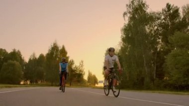 Boş alan. Gün batımında bisikletli sportif arkadaşlar. Çift bisikletçi sahil boyunca gitmek. Doğa arka planda Spor. Gün batımında iki yol bisikletçisi bir grup insan