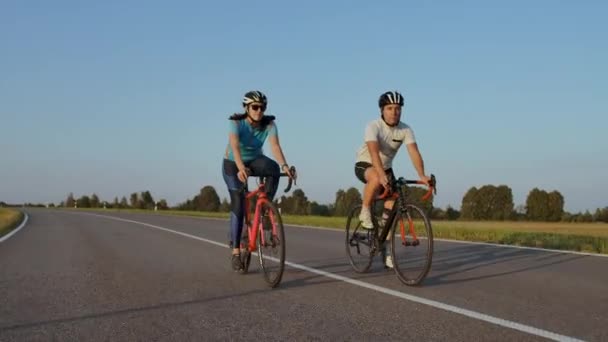 Vista frontal de una joven pareja o amigos montando sus bicicletas en el parque o bulevar de la ciudad en verano. Concepto de personas, ocio y estilo de vida . — Vídeos de Stock