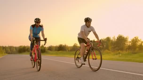 Dois ciclistas profissionais andam de bicicleta numa colina. Mão tiro realizado de dois ciclistas fortes do sexo feminino e masculino em seu treinamento em um dia quente, mas ventoso de verão . — Vídeo de Stock