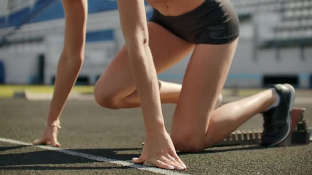 Slender young girl athlete is in position to start running in the pads on the track in slow motion. — Stock Video