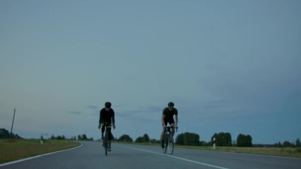 Deux cyclistes roulent sur la route le soir après le coucher du soleil. Formation tôt le matin cyclistes dans les casques . — Video