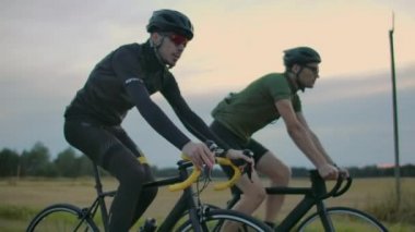 İki bisikletçi gün batımından sonra akşam yolda binmek. Kasklı bisikletçileri sabahın erken saatlerinde eğitin.