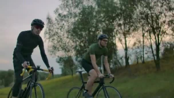 Handsome bearded professional male cyclist riding his racing bicycle in the morning together with his girlfriend, both wearing protective helmets and eyeglasses, sun shining through between them. — Stock Video