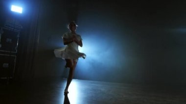 beyaz elbiseli genç bir kız mavi spot ışıklarına karşı duman ile sahnede modern bir bale dansları.