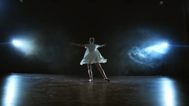 Una chica en un vestido blanco baila un ballet moderno en el escenario con humo en los focos . — Vídeo de stock