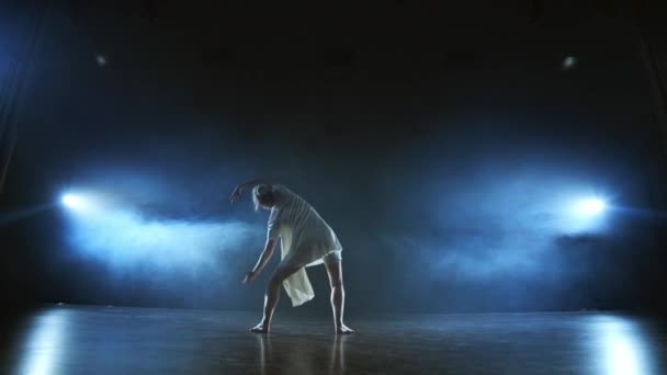 Un joven bailarín en un vestido blanco baila contemporáneo en el escenario con humo en los focos . — Vídeos de Stock