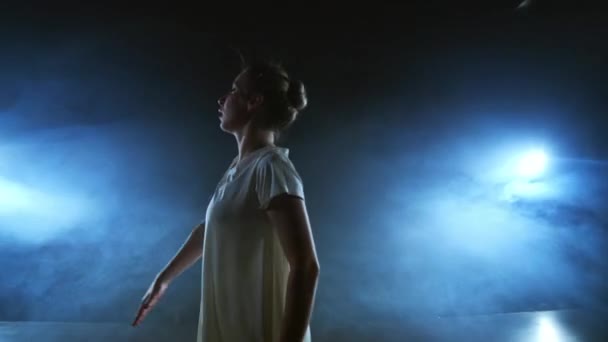 Сучасна танцювальна жінка в білій сукні танцює сучасний балет, стрибає, робить обертання на сцені з димом у блакитних прожекторах — стокове відео