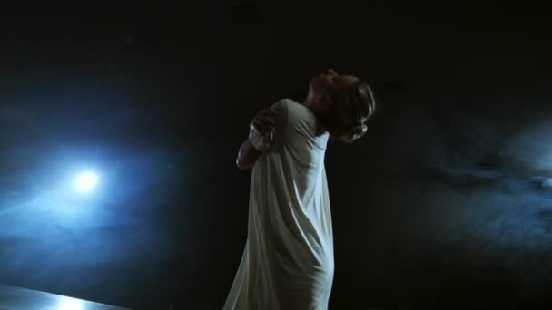 흰색 드레스를 입은 젊은 댄서가 스포트라이트를 받고 연기와 함께 무대에서 현대무용을 합니다.. — 비디오