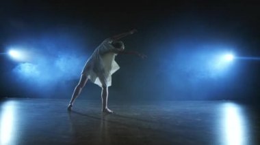 beyaz elbiseli bir kız spot ışıkları duman ile sahnede çağdaş dansları.