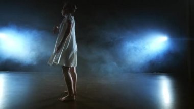 Beyaz elbiseli modern dans kız modern bir bale dansları, mavi spot ışıkları duman ile sahnede atlar.