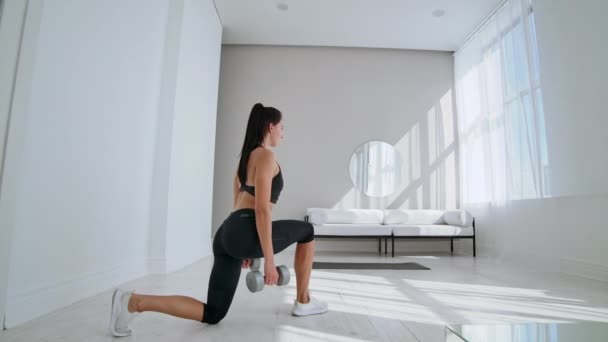 Junge, fitte und energische Frau bei Sport-Workout und Fitness-Ausfallübungen mit Gewichten für einen gesunden Lebensstil im heimischen Wohnzimmer bei sonnigem Tag. — Stockvideo