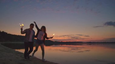 Genç mutlu çok ırklı çift yanan yanan mumlar tutarak ve gün batımında deniz tarafından çalışan. Yavaş çekim çekimi.