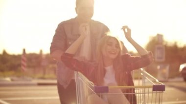 Alışveriş arabalarında dışarıda eğlenen genç bir kadın ve erkeğin yan görünümü. Çok ırklı gençler alışveriş arabalarında yarışıyor. Onların ile park alanında