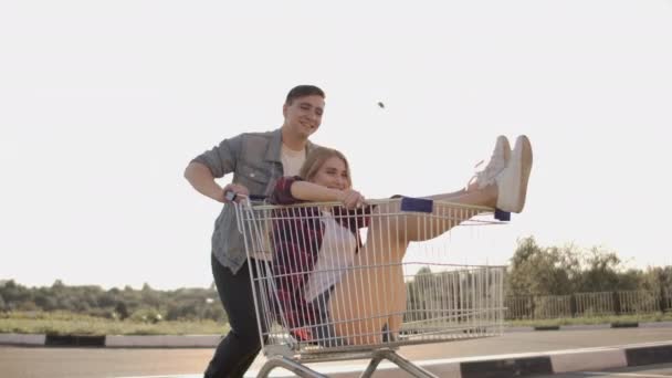 Junge Freunde amüsieren sich auf Einkaufswagen. multiethnische junge Leute, die auf Einkaufswagen rasen. Zeitlupe. — Stockvideo
