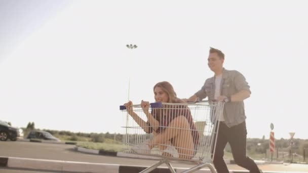 Young friends having fun on shopping trolleys. Multiethnic young people racing on shopping cart. slow motion. — Stock Video