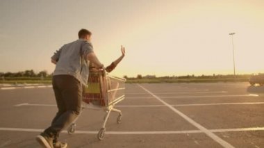 Geri görünüm. Gün batımında yavaş çekimde süpermarket park arabaları sürme ve eğlenmek aşk erkek ve kadın neşeli genç çift