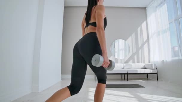 Jeune femme en forme et énergique faisant de l'entraînement sportif et des exercices de conditionnement physique avec des poids pour un mode de vie sain dans le salon à la maison pendant la journée ensoleillée . — Video
