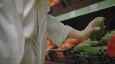 Bir kadın bir süpermarkette salatalık, sebze alarak seçiyor. alışveriş seçimi meyve, sebze satın alma. Genç kız, domates ve sebze seçen ve alan kadın. sağlık alışveriş kız